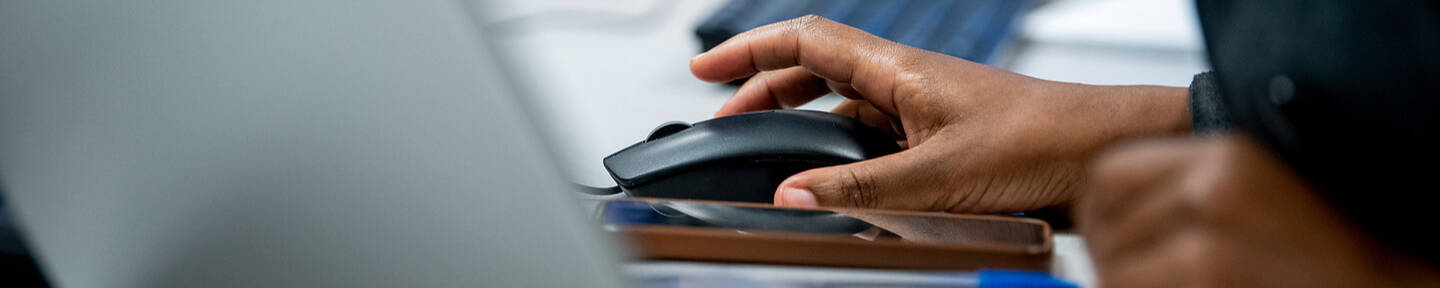 A person uses a computer mouse while working at a desk with multiple laptops.